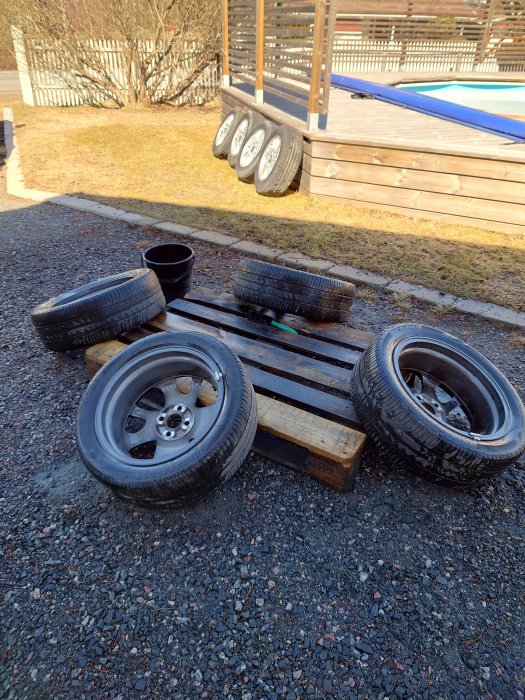 Bildäck och fälgar på marken framför en trätrall och ett hopfällbart poolskydd.