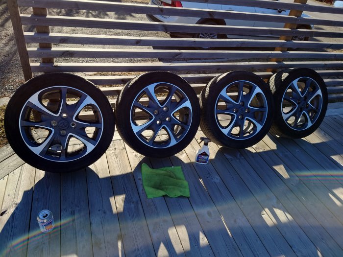 Fyra bilfälgar med däck på trägolv med rengöringsmedel och trasa.