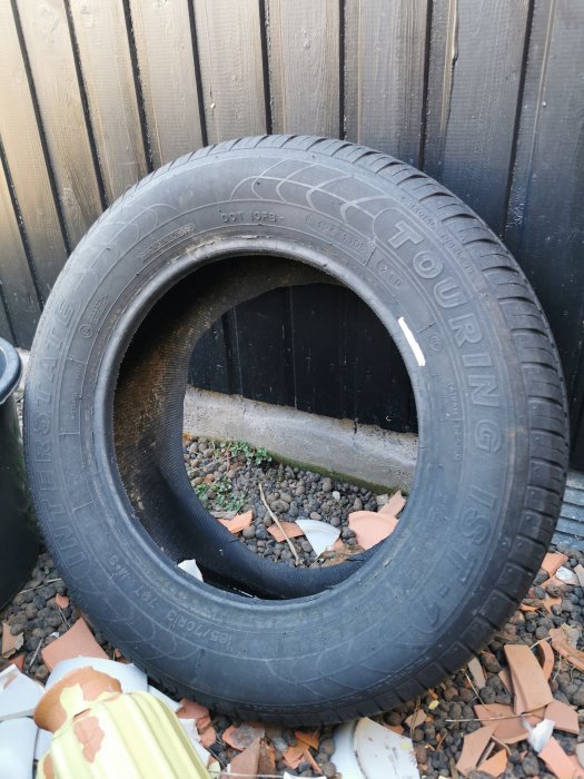 Bilddäck lutande mot en trävägg utomhus, med vissa slitna mönster synliga.