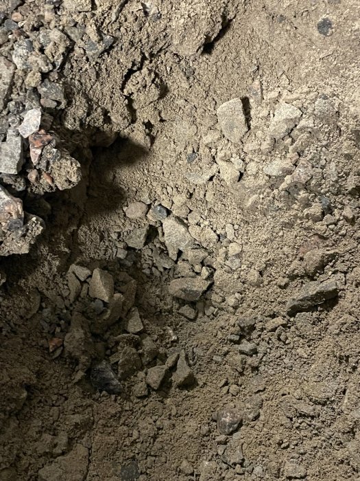 Närbild på grus och jord i provhål, ca 20 cm djupt, som diskussionsunderlag för grundläggning av garage.