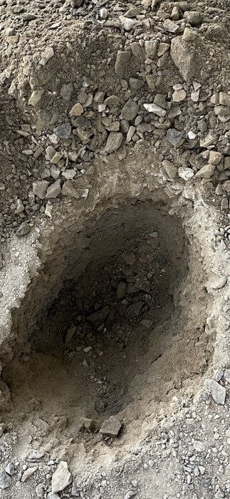 Grusig mark med ett provhål ungefär 20 cm djupt för att visa markens kvalitet inför ombildning av carport till garage.