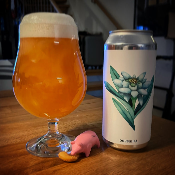 Ett glas fyllt med bärnstensfärgad öl bredvid en burk märkt "DOUBLE IPA" och en rosa dryckesmarkör.