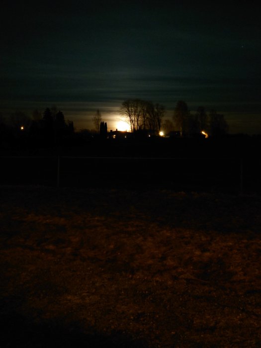 Nattbild av en fotbollsplan med upplyst horisont och månuppgång i bakgrunden.