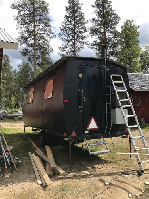 Renoverad vagn med skorsten i skogsmiljö, stege lutad mot sidan, omgiven av byggmaterial.