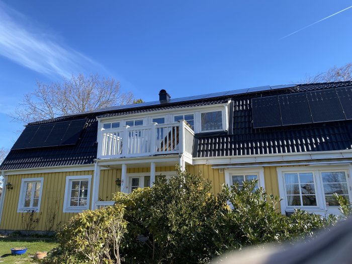 Gult hus med solcellspaneler på taket under en klarblå himmel.