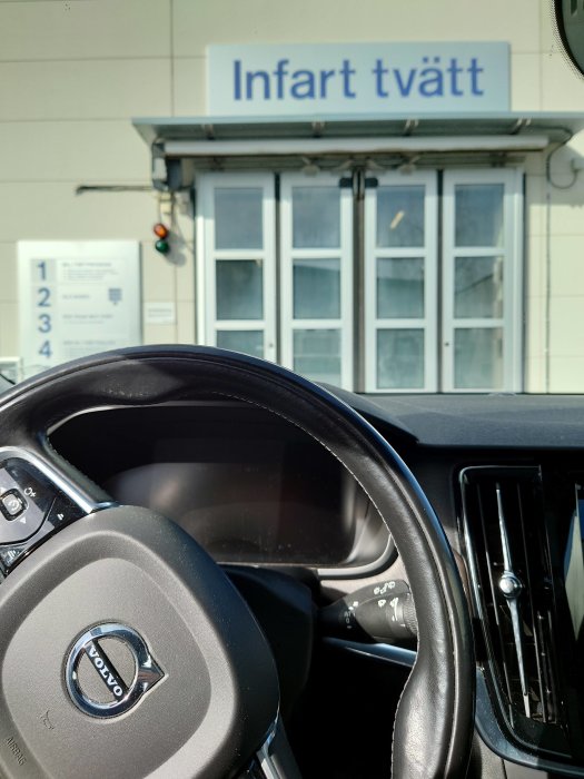 Utsikt från en bil inne i en bilkö vid infarten till en biltvätt med skylten "Infart tvätt" synlig.