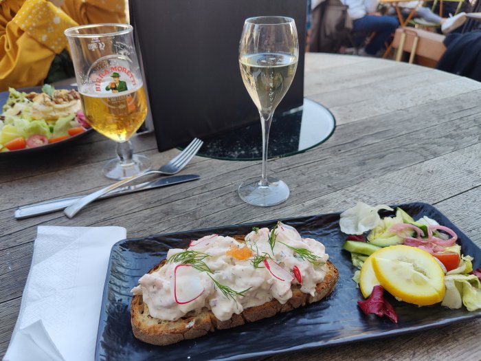 Macka med lite löjrom och dill på en svart tallrik, med sallad och ett glas vin.