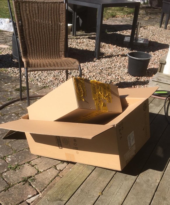 Tomma kartonger står på en trätrall i en trädgård med trädgårdsmöbler i bakgrunden.