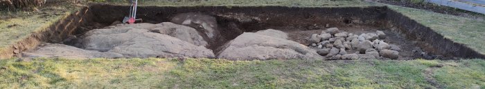Utgrävning för växthus på bergsgrund, med synligt berg och jord, samt en spade och hög med stenar.
