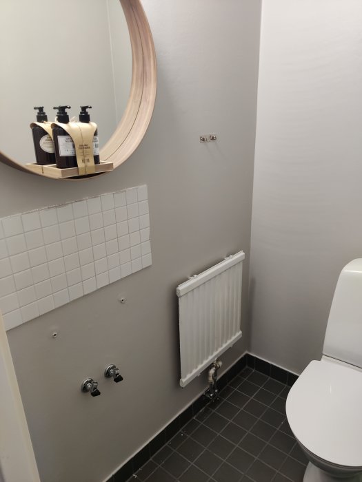 Nyrenoverad toalett med grå väggar, vit kakelsockel, svart klinkergolv och väggmonterade kranar.