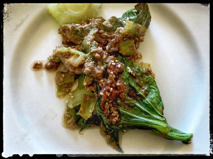 Lätt lunch på en vit tallrik med pak choi täckt i sesamfrösås.