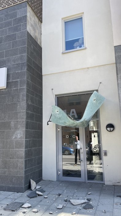 Skadat partier i en byggnad med krossade fönsterglasbitar och trasigt skyltfönster på trottoaren.
