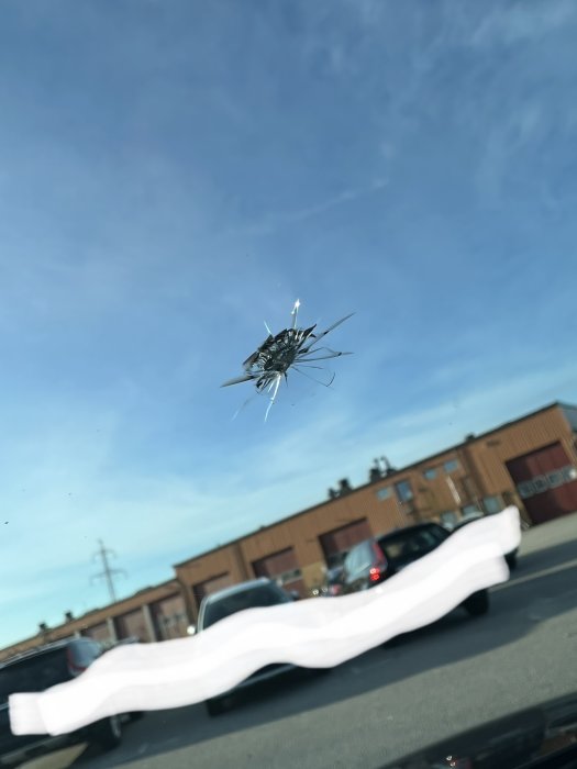 Stenskott i bilruta med sprickor mot en bakgrund av parkerade bilar och byggnader.
