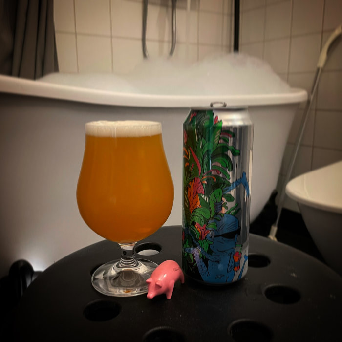 Ölglas och burk på badrumsbord framför skumfyllt badkar med liten plastgris.