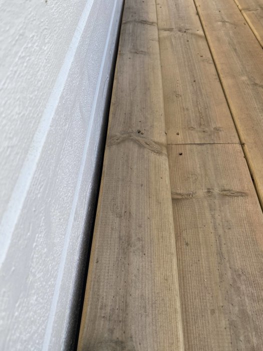 Altanbräda nära husvägg med litet mellanrum och synlig fuktighet på underliggande yta.