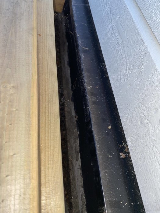 Altanbräda borttagen nära husvägg, visar mellanrum och delvis fuktig husgrund.