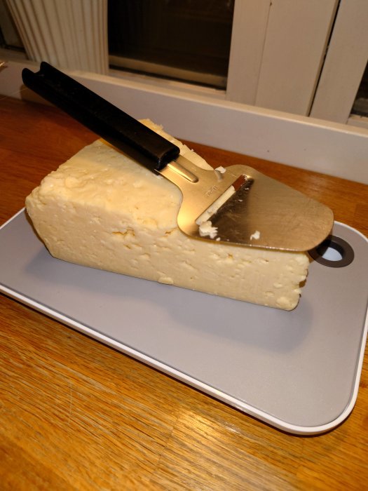 Ett stort stycke ost på en skärbräda med en osthyvel uppstickande från osten.