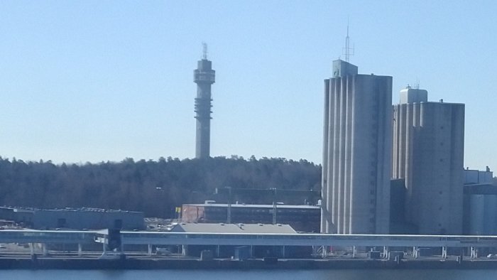 Stadsbild med torn och industribyggnader vid vattnet under klart väder.