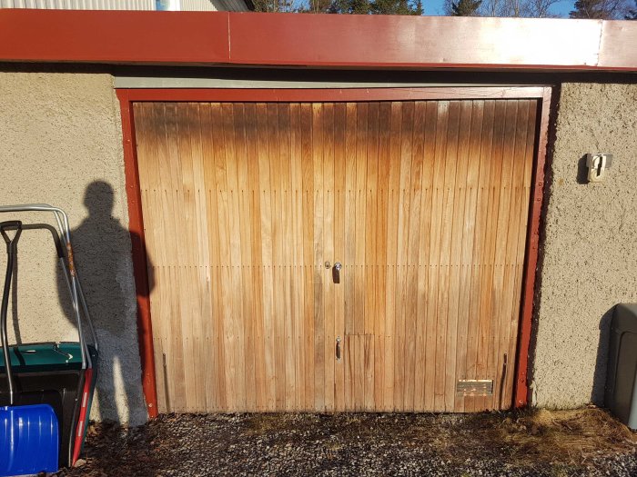 Nedmonterad trävipport med synlig slitage och några bultar saknas, mot en garagevägg.