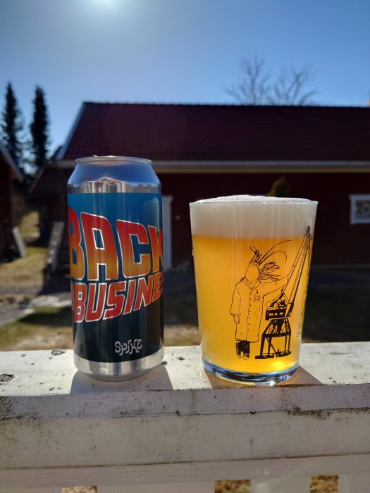 Ölburk och glas med öl på ett staket med soligt hus i bakgrunden.
