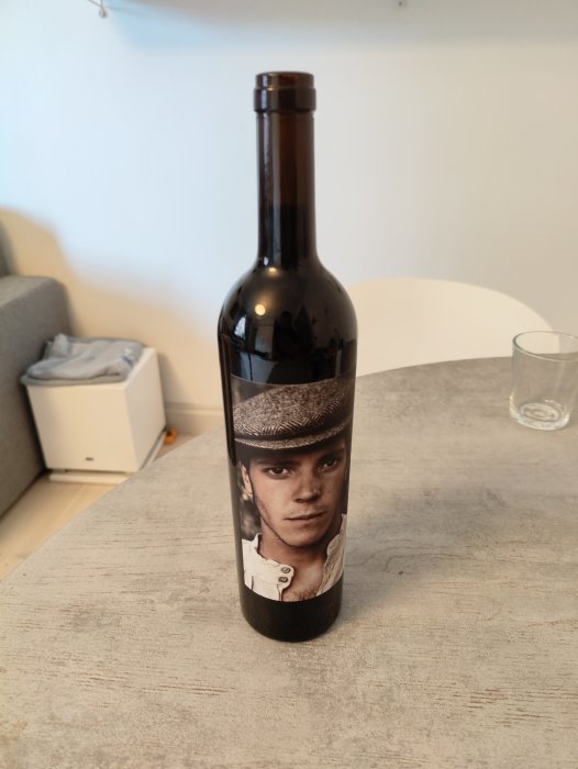 Flaska vin på bord med bild av ung man på etiketten, där bakgrunden är en heminteriör.