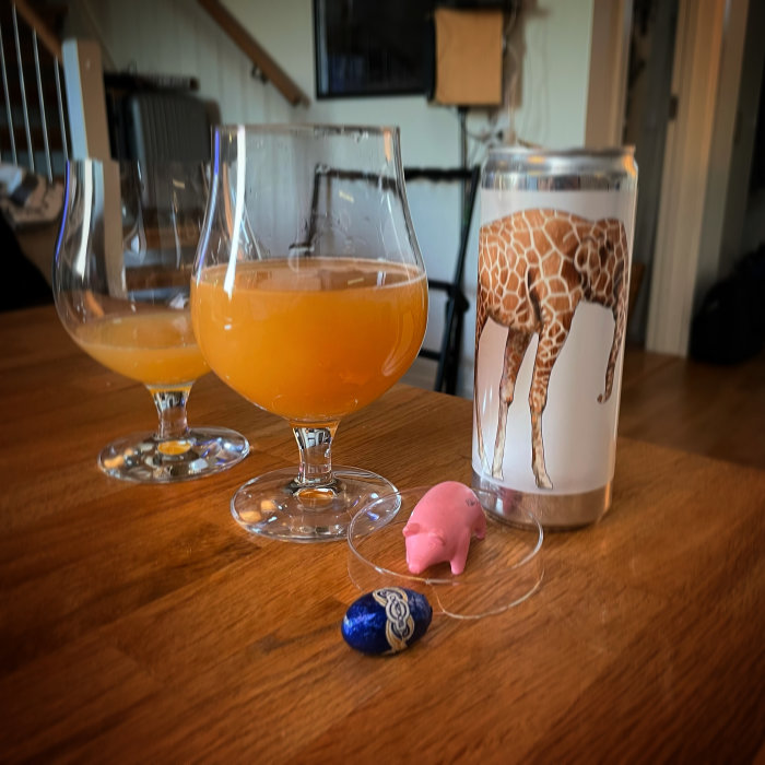 Två glas med orange dryck, en stressleksak i form av en rosa gris och en burk med giraffmotiv på ett bord.