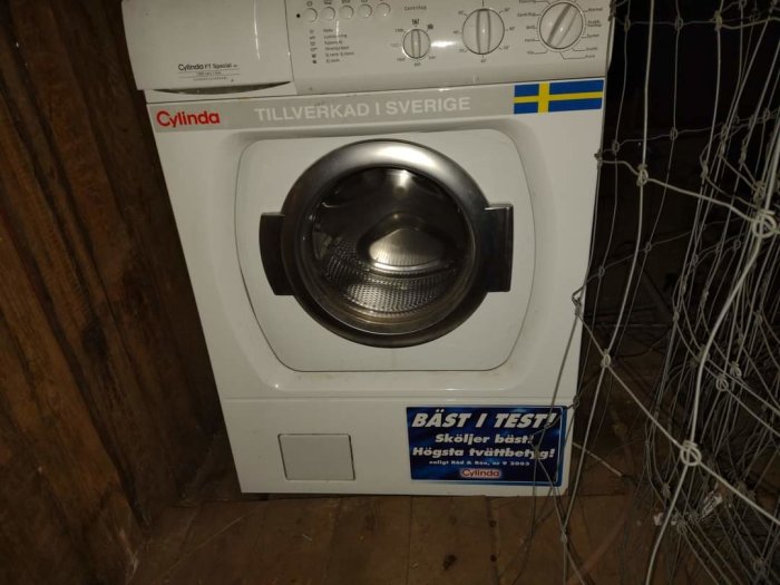 En äldre Cylinda tvättmaskin modell FT 517 med svenska flaggan och "Bäst i Test" klistermärke, placerad i ett mörkt rum.