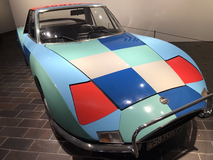 Klassisk bil med färgglatt rutigt mönster på karossen, utställd på mörkgrått golv.