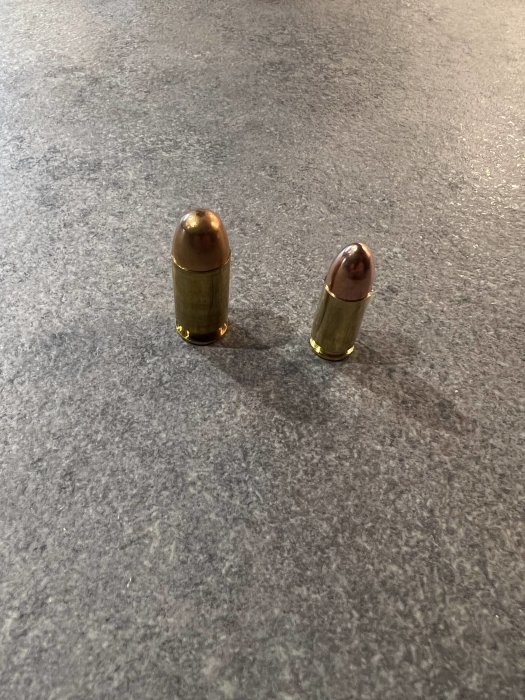 Två ammunitionspatroner står på en mörk texturerad yta.