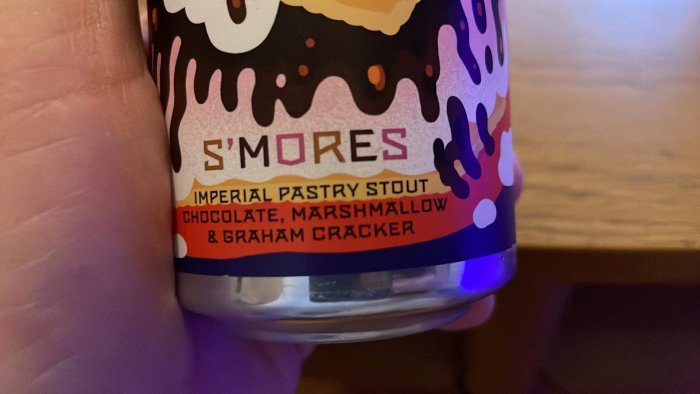 En hand håller en ölburk med texten "S'MORES IMPERIAL PASTRY STOUT" och smakbeskrivningar.