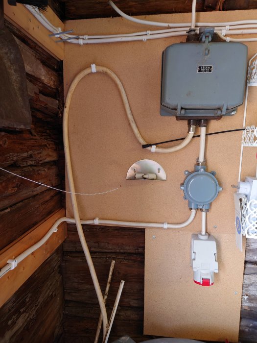 Elanläggning i ett gammalt träskjul med kabeldragningar, dosor och en gammal säkerhetsbrytare på en spånskivevägg.