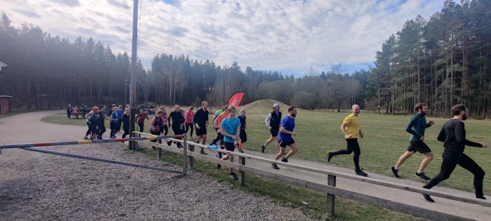 Grupp löpare i färgglada kläder som startar ett Backyard-ultramaraton i skogsmiljö.