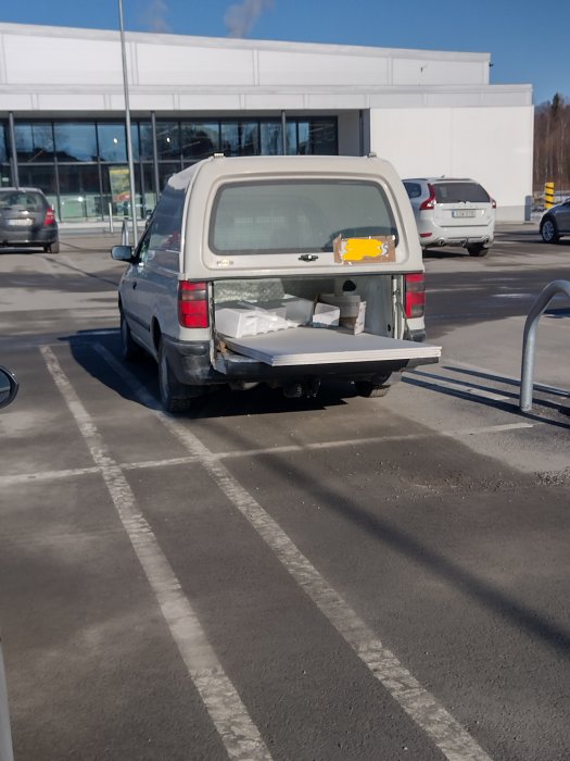 En vit skåpbil med öppen bakdörr parkerad utanför en byggnad, lastad med verktygslådor och material.