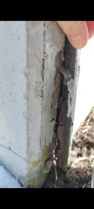Skadad mjukfog på en vitmålad betongsockel där fogen lossnat och exponerar en springa under huset.