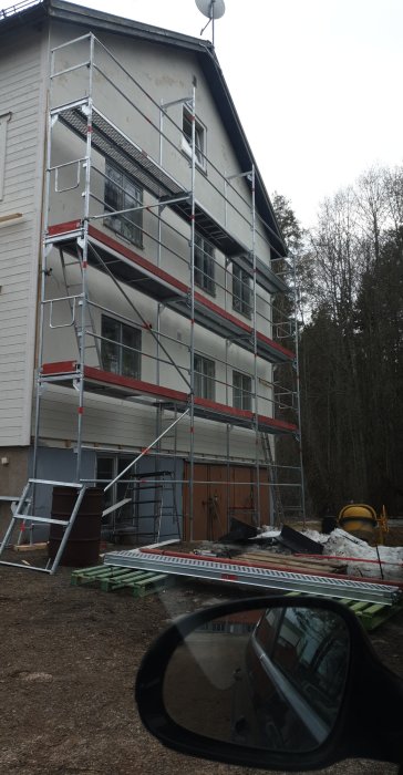 Ställning uppställd mot en flervåningsbyggnad med ofärdigt arbete och byggmaterial nedanför.