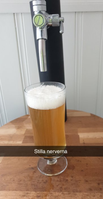 Ett ölglas med öl står på ett träbord med texten "Stilla nerverna" under.
