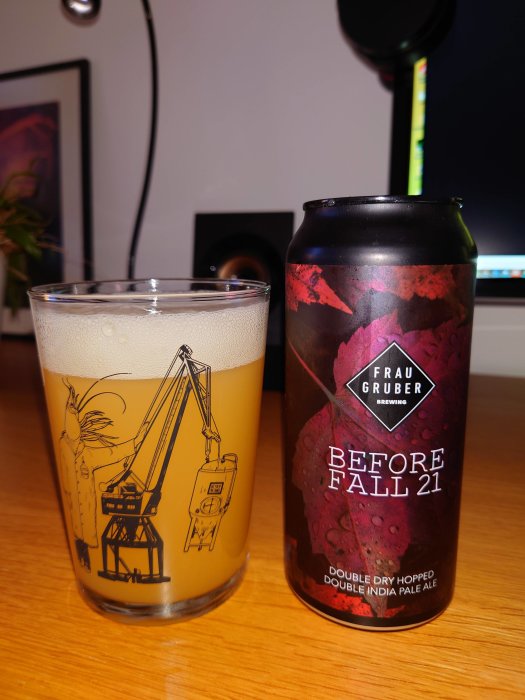 Ölglas med illustrationer bredvid en burk "Before Fall 21" Double IPA, på ett bord framför en datorskärm.