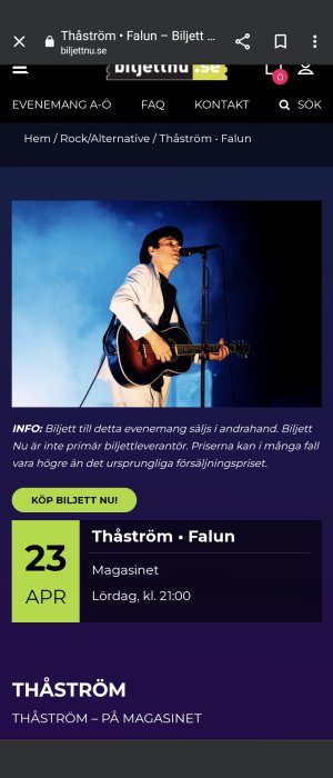 Musiker i kostym spelar gitarr och sjunger i mikrofon på scen med blå bakgrund.