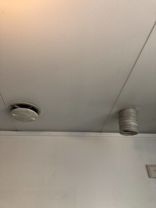 Vy av ett vitt tak med två ventilationskanaler, varav en är en amatörmässig anslutning med synligt rör.