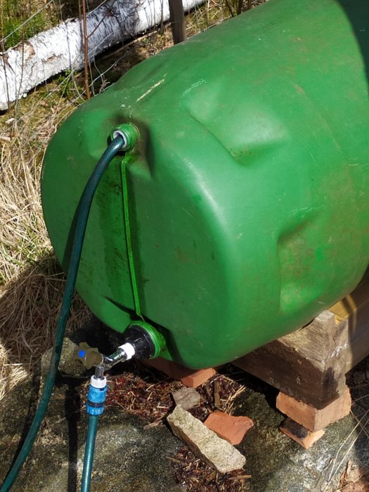 Grön vattentunna med monterad adapter och ansluten slang med kran för växthusbevattning.