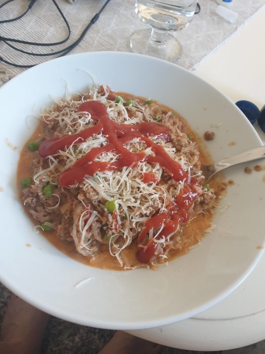 Tallrik med köttfärssås och konjakrotsnudlar toppade med riven ost och ketchup.