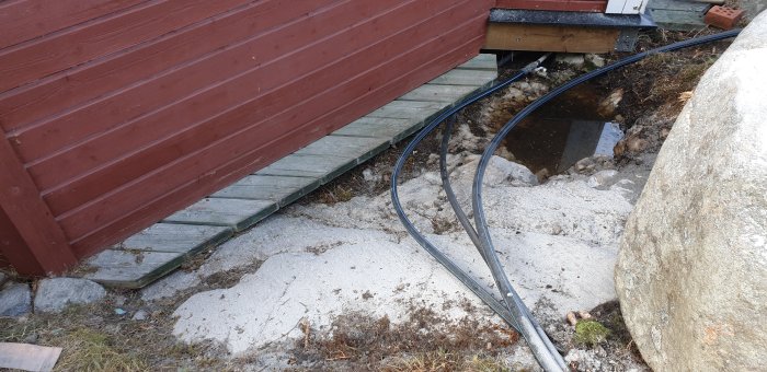 Berg nära byggnad och trätrall med borrutrustning och slangar som förberedelse för bergsprängning.