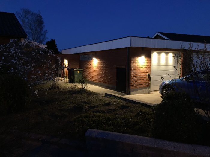 Garage med tänd utebelysning i skymningen, belysningens ljus speglas på garageporten.