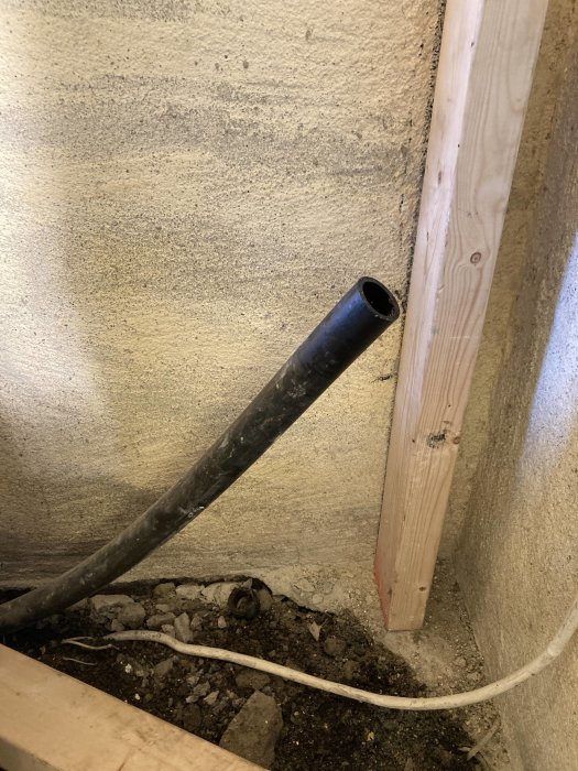 Svart rör med ca 28 mm invändig och 37 mm utvändig diameter sticker ut vid en betongvägg och träregel.