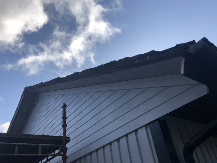 Takrenovering på hus med vit fasad och svart takbeklädnad under blå himmel med moln.