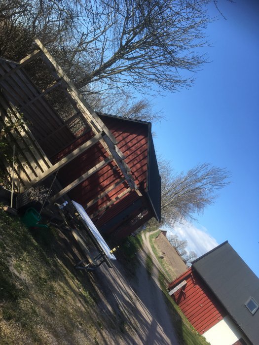 Ett landskap med röda trädgårdsbyggnader och ett picknick-bord, med träd och klar himmel i bakgrunden.