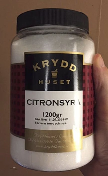 En hand håller en burk med märkningen "KRYDDHUSET CITRONSYRA 1200g".