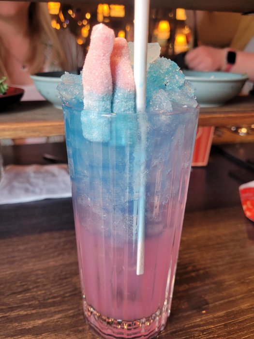 Ett cocktailsugrör i ett glas med en lagerdelad dryck och sockrade godisar på toppen.