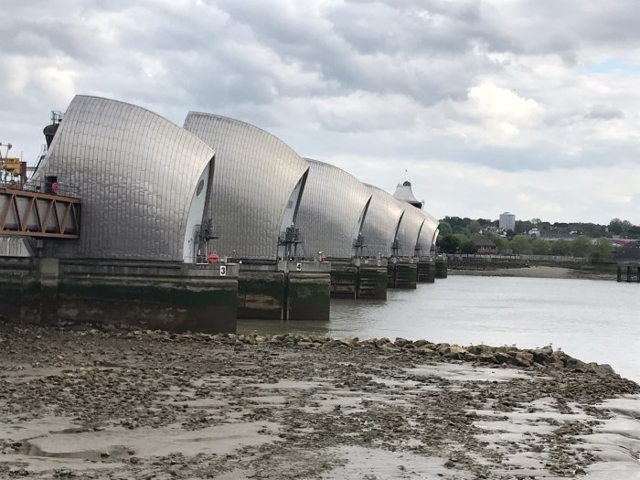 Modern barriär vid flod med böjda metallstrukturer och lågvatten som visar flodbädden.