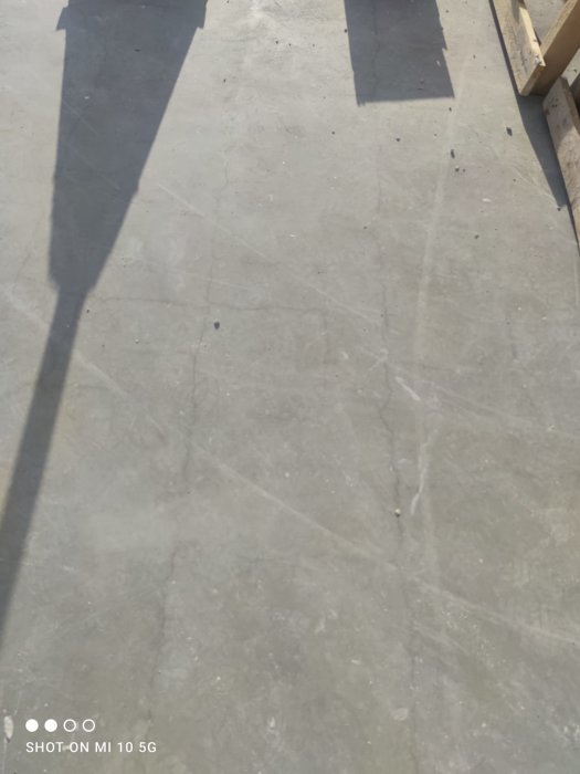 Rektangulär betongyta med skuggor och sprickbildning samt nedre delen av ett trädäck.